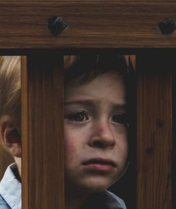 Saúde mental das crianças: na imagem, um bebê olha entre grades de madeira com uma expressão de tristeza
