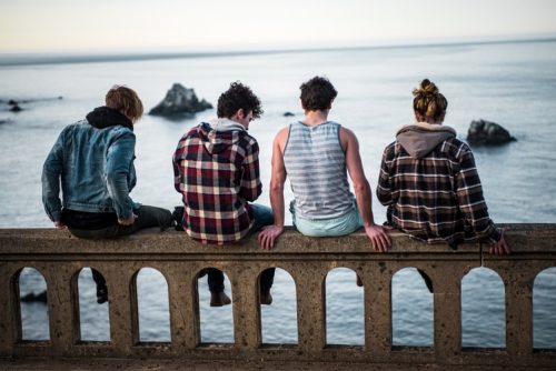 Automutilação e suicídio: como abordar? Na imagem, um grupo de adolescentes está sentado em uma ponte, de frente para um rio. São três meninos e uma menina e todos estão com roupas casuais.